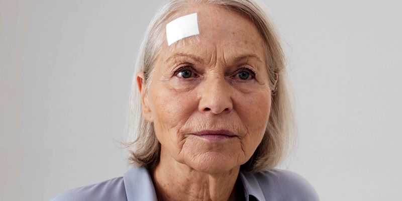 Close up of gloved hands gently removing a wound dressing from an elderly woman's arm  Close up of gloved hands gently removing a wound dressing from an elderly woman's arm